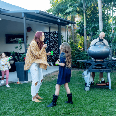 Family playing in the backyard while Dad looks after the BBQ